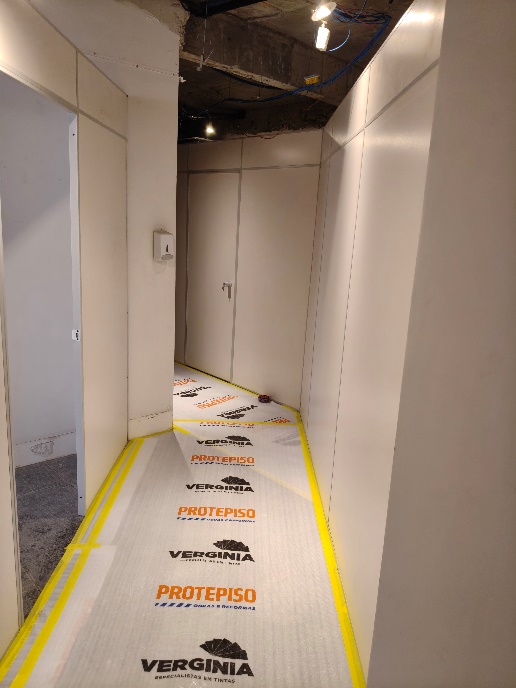 Corredor de acesso com proteção de piso e demarcação para circulação segura.